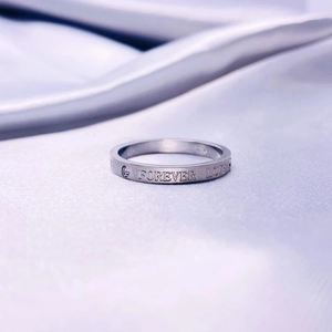 Primer plano del anillo de plata con grabado Forever Love sobre seda color púrpura