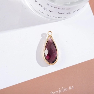 Macro shot of faceted teardrop purple crystal pendant with gold-plated metal border