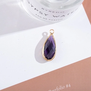 Detailed close-up of a purple teardrop crystal pendant with gold-plated metal frame