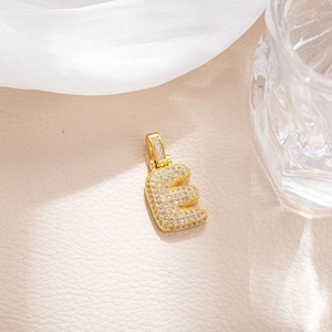 Macro shot of gold E pendant with micro-pave white cubic zirconia on beige leather