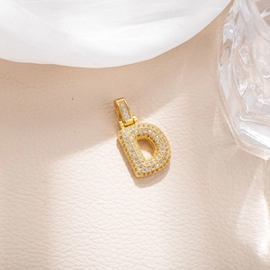Macro shot of gold micro-pave letter D pendant with sparkling zircon on beige leather