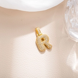 Macro detail of gold-plated bubble letter R pendant with sparkling zircon inlay