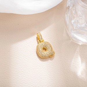 Detail of gold plated letter Q pendant with cubic zirconia on beige leather background