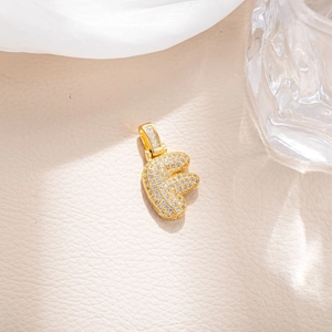 Macro shot of gold-plated letter F pendant with micro-pave cubic zirconia on leather