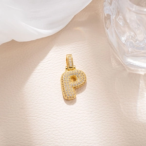 Macro detail of gold letter P pendant featuring pavé-set zircons on textured background