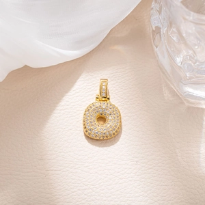 Detail of gold letter O pendant with pave cubic zirconia on beige leather background
