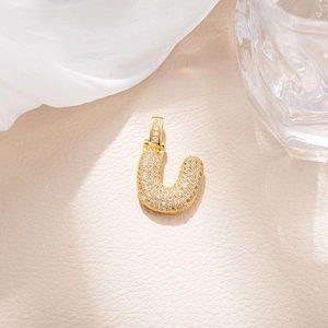 Detailed close-up of golden letter U pendant with micro-pave zircons on leather