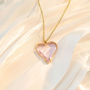 Details einer rosafarbenen Herz-Kristallkette mit Goldkette auf weißer Seide