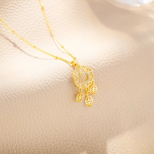 Macro shot of gold dreamcatcher pendant with leaf charms on a textured leather background