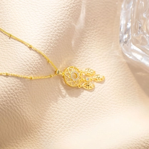 Detailed close-up of golden dreamcatcher necklace with leaf charms on beige leather
