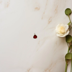 Detail of a red teardrop zircon pendant with gold rim and elegant white rose on marble