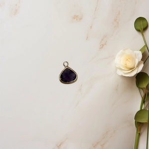 Macro shot of purple faceted teardrop pendant with gold bezel on marble surface