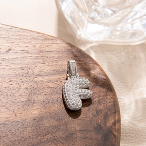 Detailed view of silver letter F pendant with pave-set cubic zirconia on walnut wood