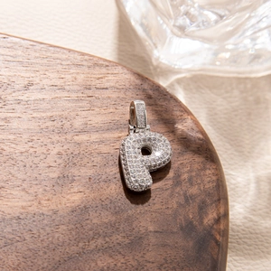 Macro shot of silver letter P pendant with micro-paved zircons on a wooden display