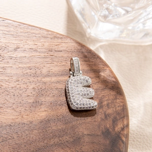Macro shot of silver letter E pendant with micro-pave white zircon inlay on wood surface