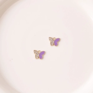 Dettaglio di ciondoli a farfalla dorati con smalto viola e cristalli pavé su piatto ceramico