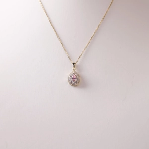 Elegant gold pear-cut pink sapphire pendant necklace with halo crystals on white bust