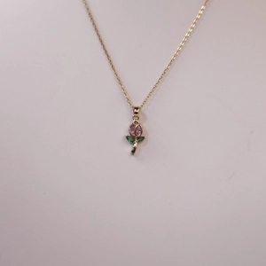 Collar dorado con colgante floral de cristales rosas y verdes sobre fondo gris suave