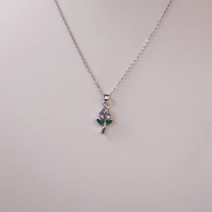Detalle del colgante de flor con circón blanco y gemas verdes en una fina cadena de plata