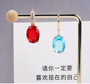 Detailed view of asymmetric oval crystal earrings with gold plating and paved rhinestones