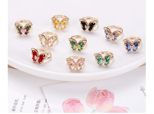 Multiple colors of 18K gold butterfly rings with crystal stones on a ceramic tray