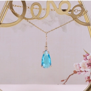Detailed close-up of light blue teardrop crystal pendant in gold four-prong setting