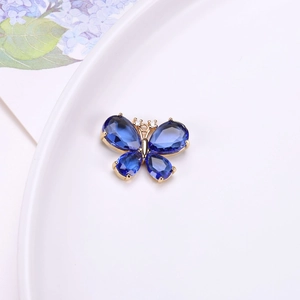 Primer plano de un colgante de mariposa de cristal azul con engaste dorado en bandeja blanca