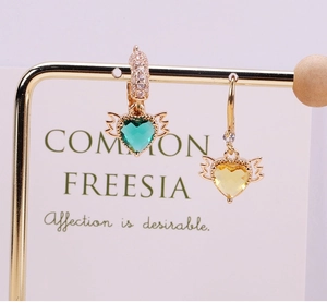 Detail showing heart-shaped crystal wings charms in green and yellow gold plating