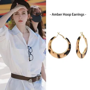 Detail view of multi-layer amber resin and gold metal C-shape hoop earrings on model