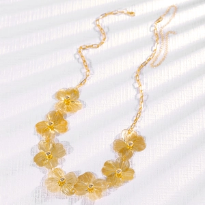 Detail van bohemien gouden frangipani bloem tailleketting met geborsteld metaal textuur