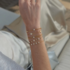 Close-up view of five dainty gold-plated bracelets featuring white zircon clover charms on a female wrist