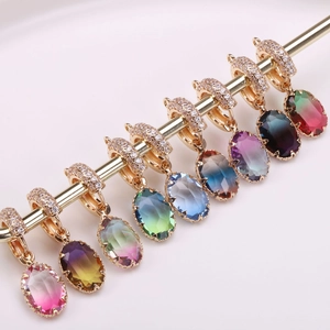 Gradient oval crystal pendants with gold zirconia bails displayed on a metal stand