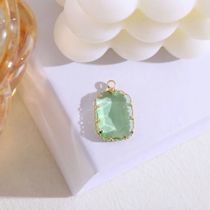 Detalle de colgante de cristal verde rectangular con engaste de corona dorada