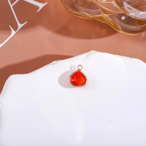 Close-up of a faceted red teardrop crystal pendant with gold setting on white rock