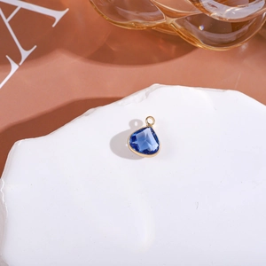 Macro shot of faceted blue teardrop crystal pendant with gold rim on white stone