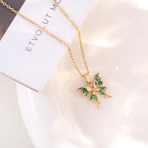 Macro shot of gold butterfly necklace with green zircon inlay on a ceramic tray