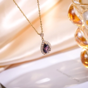 Macro detail of tear-drop pendant with purple gem and white diamonds on gold chain