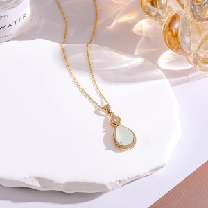 Macro shot of gold plated teardrop pendant with pale green stone and zircon inlay