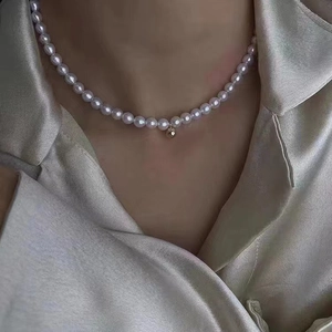 Elegant pearl necklace with gold heart pendant worn on silk shirt for women