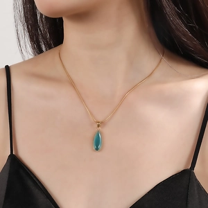 Dettaglio della collana a goccia dorata con gemma verde indossata da una modella