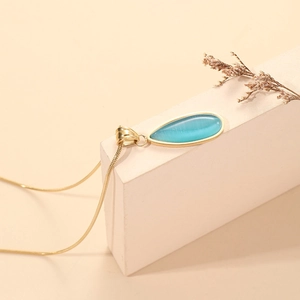 Elegante collar de gota de oro con piedra de ojo de gato azul sobre pedestal de piedra