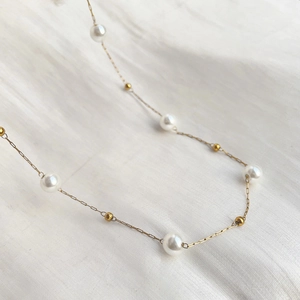 Detailed macro view of minimalist pearl necklace with gold chain on white fabric background