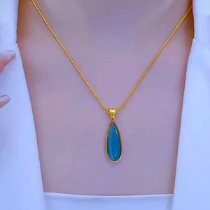 Elegante collar de oro con un colgante de gota azul sobre una chaqueta blanca