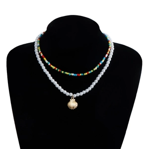 Detail of double-layer beaded necklace with faux pearls and golden shell pendant charm