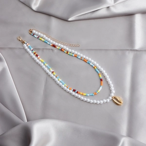 Detail view of double-layer beaded necklace with faux pearls and shell pendant on satin
