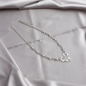 Detail of silver thorn heart pendant and barbed wire chain on grey satin background