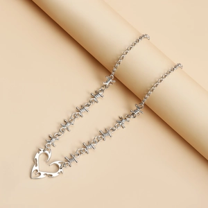 Detail of silver spiked heart pendant and barbed wire chain necklace in Y2K style