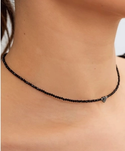 Detailopname van een zwarte kralen choker met een zilveren hart hanger bij een model