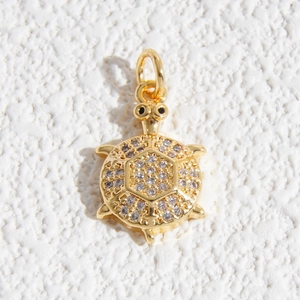Dettaglio di un ciondolo a forma di tartaruga dorata con cristalli e anello superiore