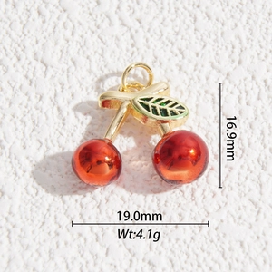 Detailed macro view of gold plated cherry pendant with green enamel leaf and red resin spheres